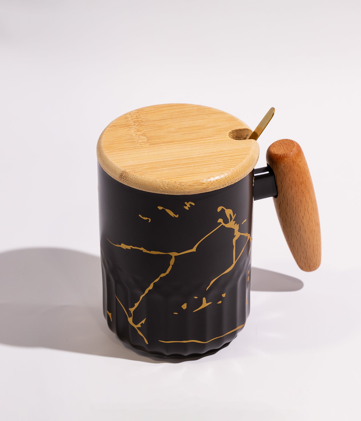 كوب مصنوع من السيراميك باللون الأسود مزين بعروق ذهبية أنيقة، مزود بمقبض وغطاء خشبي وملعقة، مناسب للاستخدام اليومي مع القهوة أو الشاي