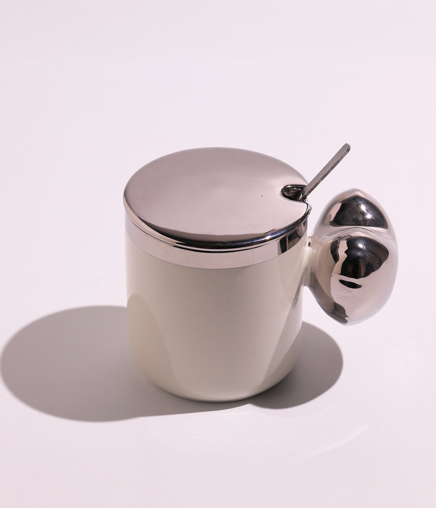 كوب سيراميك بتصميم أنيق مع مقبض فريد، مزود بغطاء فضي وملعقة، باللون الأبيض