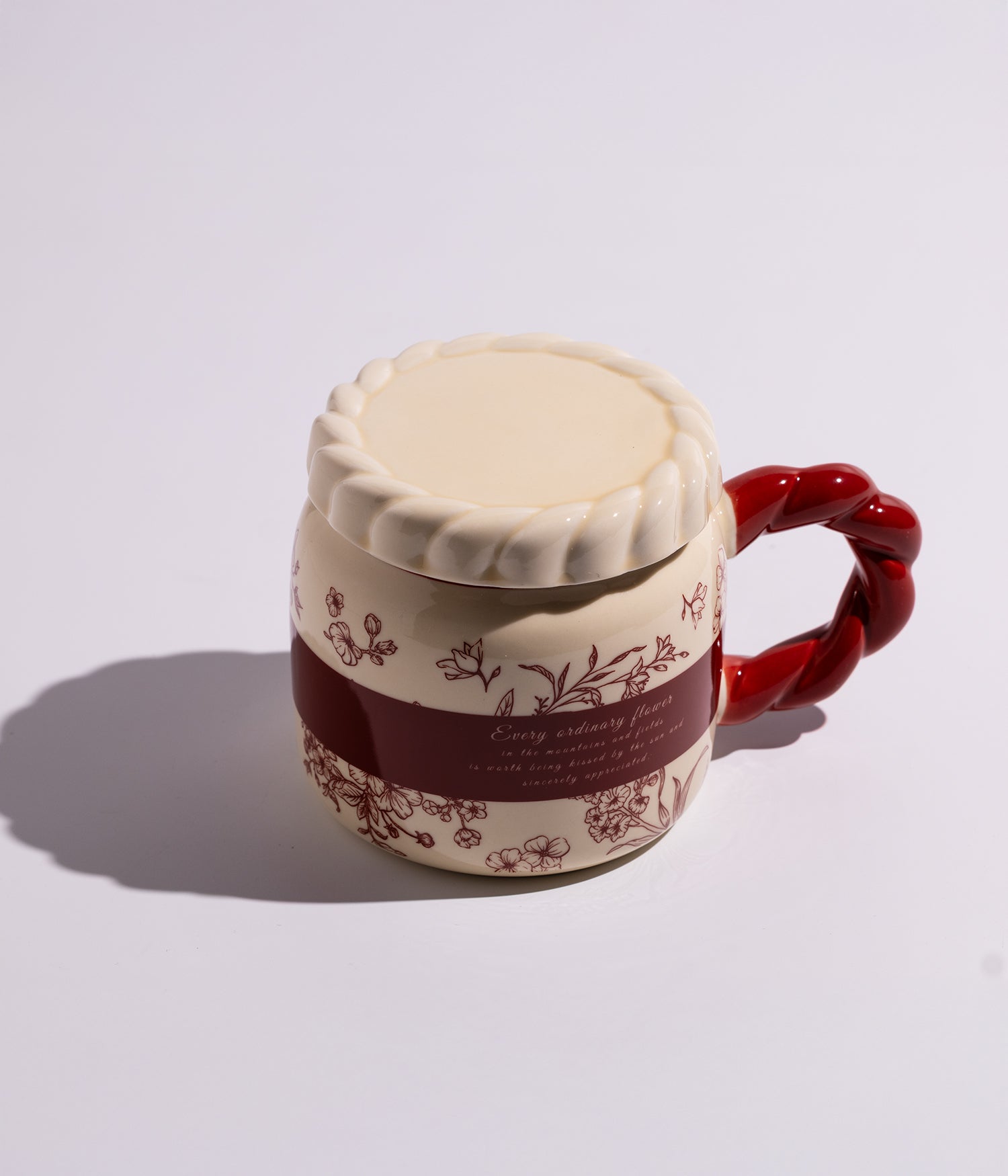 كوب سيراميكي مزخرف بورود ملونة، يحتوي على مقبض أحمر وغطاء محكم الإغلاق، ملائم للاستخدام اليومي في المنزل أو المكتب