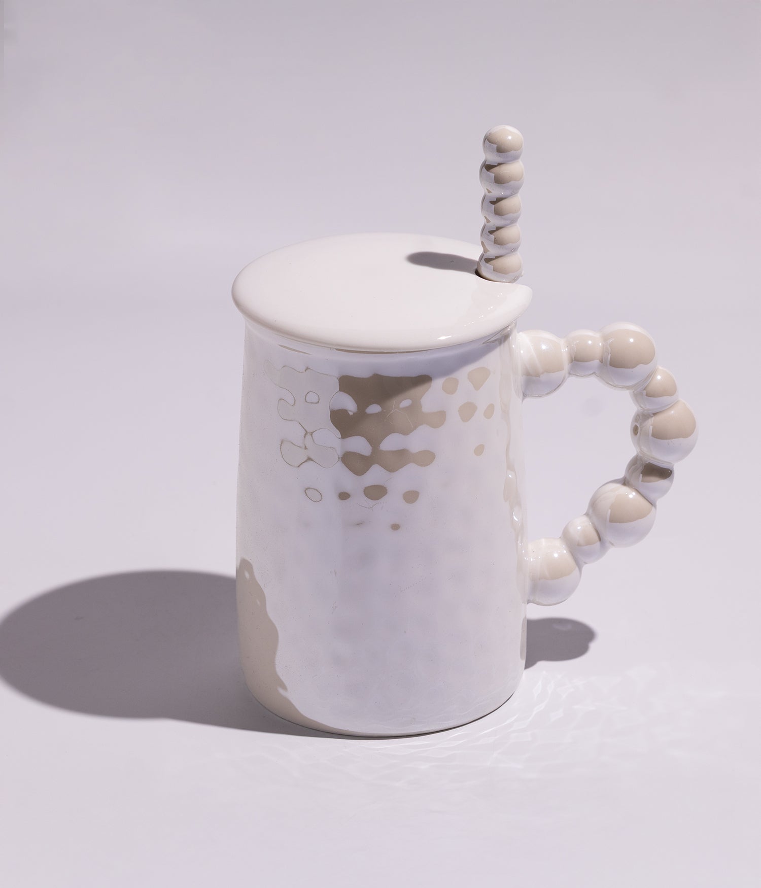 كوب قهوة مصنوع من السيراميك بمقبض بتفاصيل لؤلؤية أنيقة ويأتي مع غطاء وملعقة باللون الأبيض