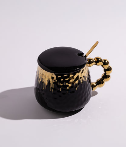 كوب مصنوع من السيراميك باللون الأسود مزين بزخارف ذهبية وتصميم لؤلؤي، مزود بغطاء وملعقة، مناسب للاستخدام اليومي مع القهوة أو الشاي