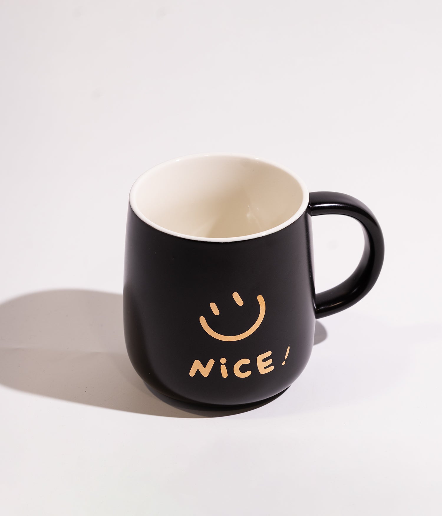 كوب مصنوع من السيراميك بتصميم وجه مبتسم مع كلمة NICE، يأتي باللون الأسود ومزود بغطاء لحفظ الحرارة وملعقة، مناسب للاستخدام اليومي مع المشروبات الساخنة