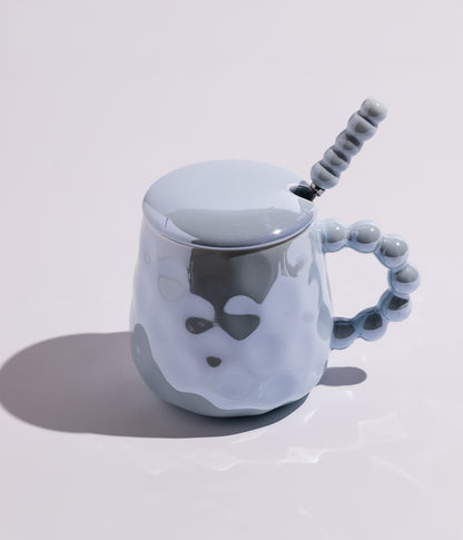 كوب من السيراميك باللون الأزرق، مزود بمقبض لؤلؤي فريد مع غطاء وملعقة، مناسب لتقديم المشروبات الساخنة