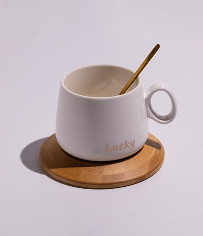 فنجان سيراميك بعبارة «LUCKY» مع قاعدة خشبية دائرية وملعقة بلون أبيض