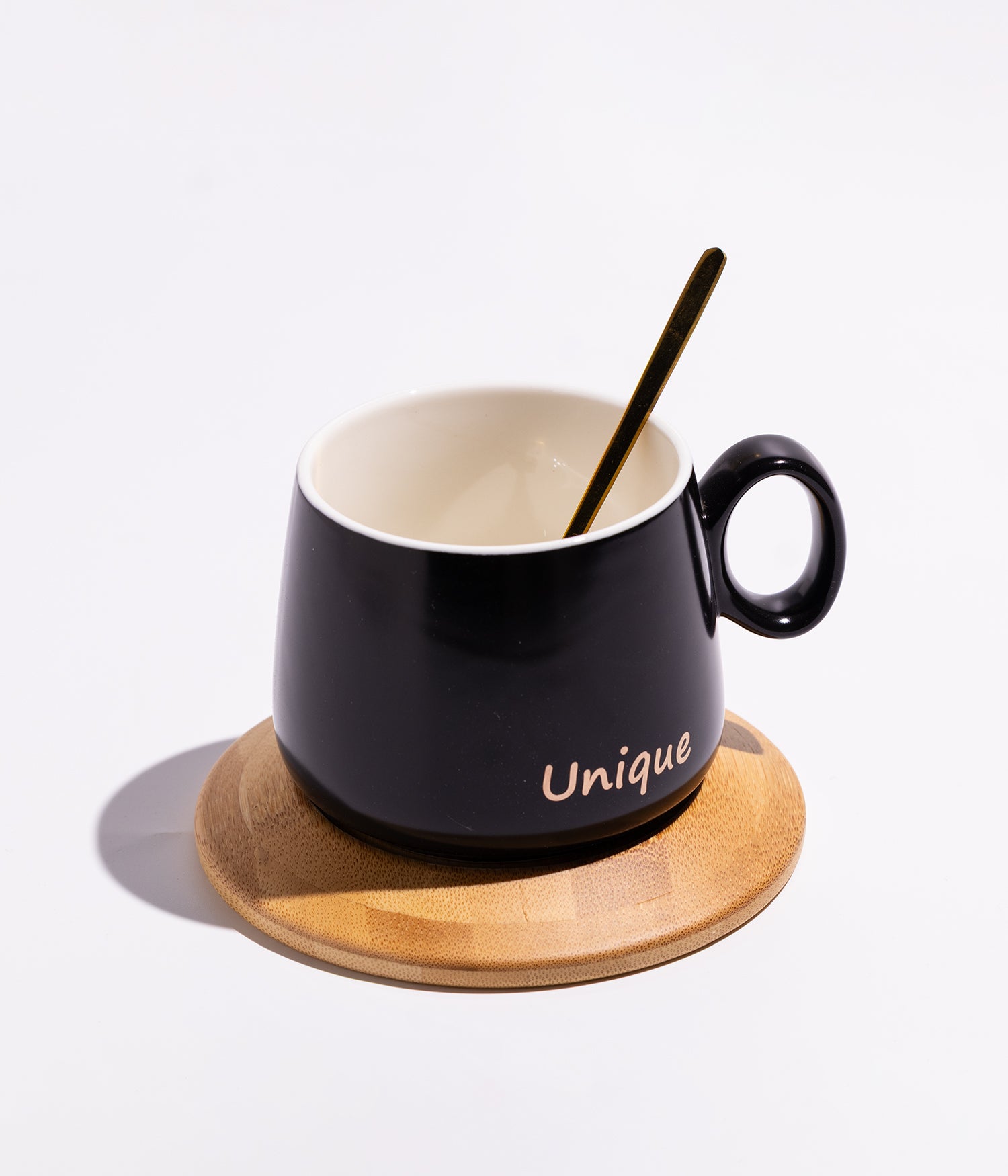 فنجان سيراميك بعبارة «UNIQE» مع قاعدة خشبية دائرية وملعقة بلون أسود