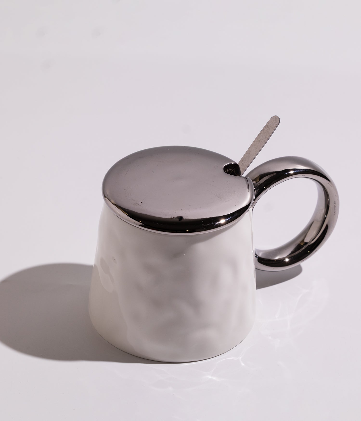 كوب سيراميك بتصميم أنيق مع غطاء ومقبض ميتاليك، مرفق بملعقة معدنية ملونة، باللون الأبيض مع غطاء فضي
