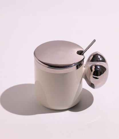 كوب سيراميك بتصميم أنيق مع مقبض فريد، مزود بغطاء فضي وملعقة، باللون الأبيض
