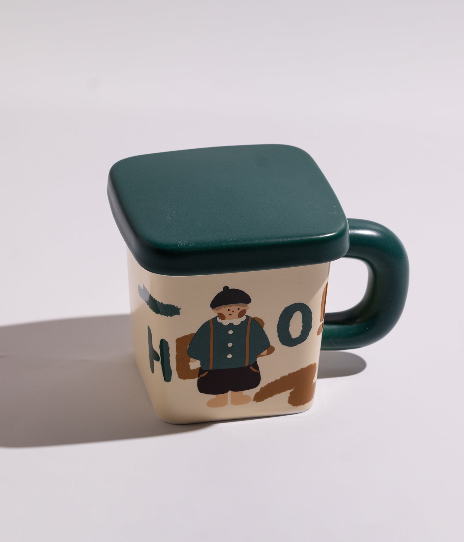 كوب سيراميكي مزين بشخصيات مرحة، يأتي مع غطاء أخضر محكم الإغلاق، مناسب للاستخدام اليومي مع القهوة أو الشاي