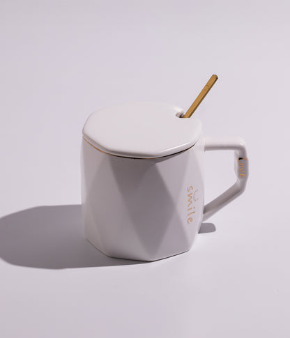 كوب سيراميك بتصميم أنيق مزين بلمسة ذهبية، مع غطاء وملعقة، وعبارة SMILE مكتوبة باللون الذهبي، باللون الأبيض