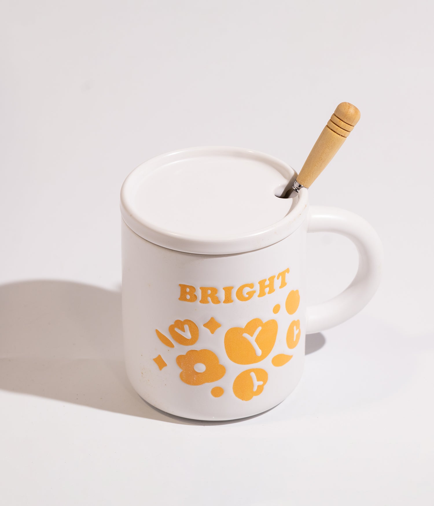 كوب من السيراميك بتفاصيل ورود ملونة ولمسة لونية برتقالية هادئة مزود بغطاء مناسب وملعقة خشبية ليمنح استخدامًا عمليًا وشكلًا متوازنًا يناسب تقديم المشروبات الساخنة ويضيف مظهرًا أنيقًا للمكان