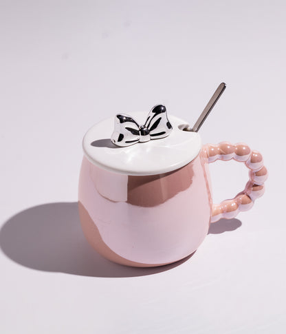 كوب سيراميكي باللون الوردي مصنوع من خامة عالية الجودة، مزود بغطاء بتصميم بابيون ومقبض لؤلؤ مع ملعقة مرفقة، مناسب للقهوة أو الشاي وخيار مناسب للهدايا
