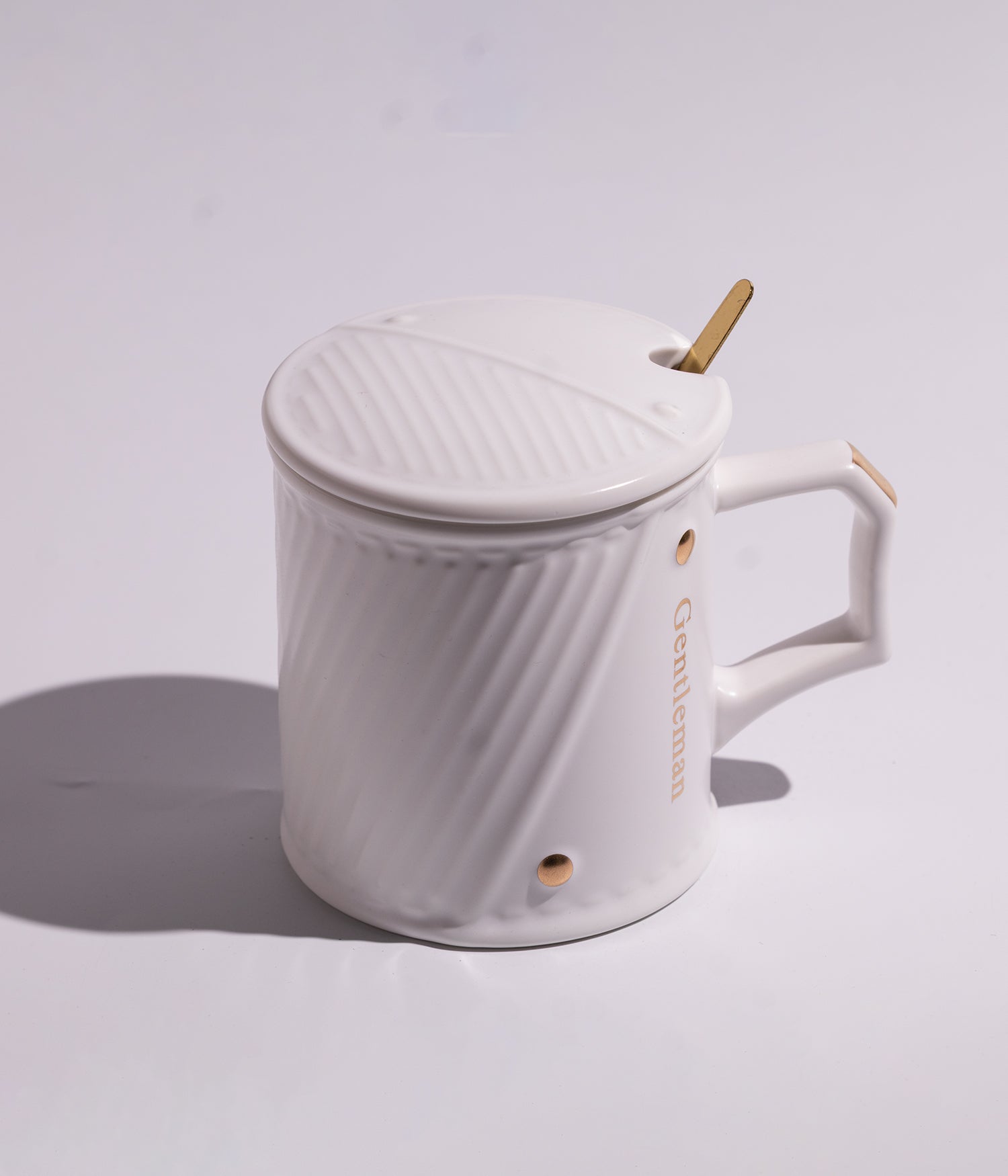 كوب قهوة مصنوع من السيراميك بتصميم خطوط مائلة أنيقة باللون الأبيض، مزود بغطاء وملعقة، مناسب للاستخدام اليومي مع القهوة أو الشاي