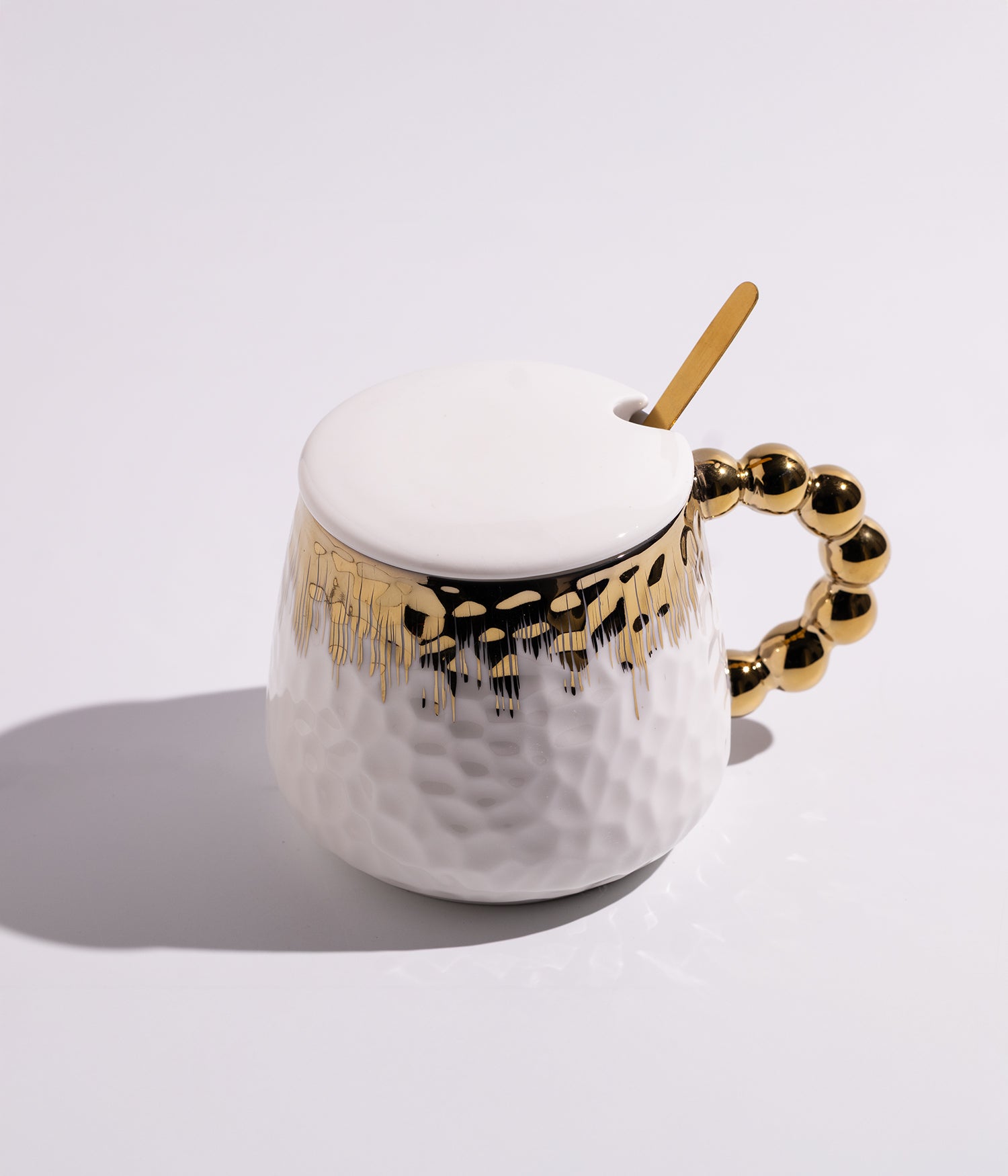 كوب سيراميكي باللون الأبيض مزخرف بزخارف ذهبية وتصميم لؤلؤي أنيق، يأتي مع غطاء وملعقة، ملائم للاستخدام اليومي في المنزل أو المكتب