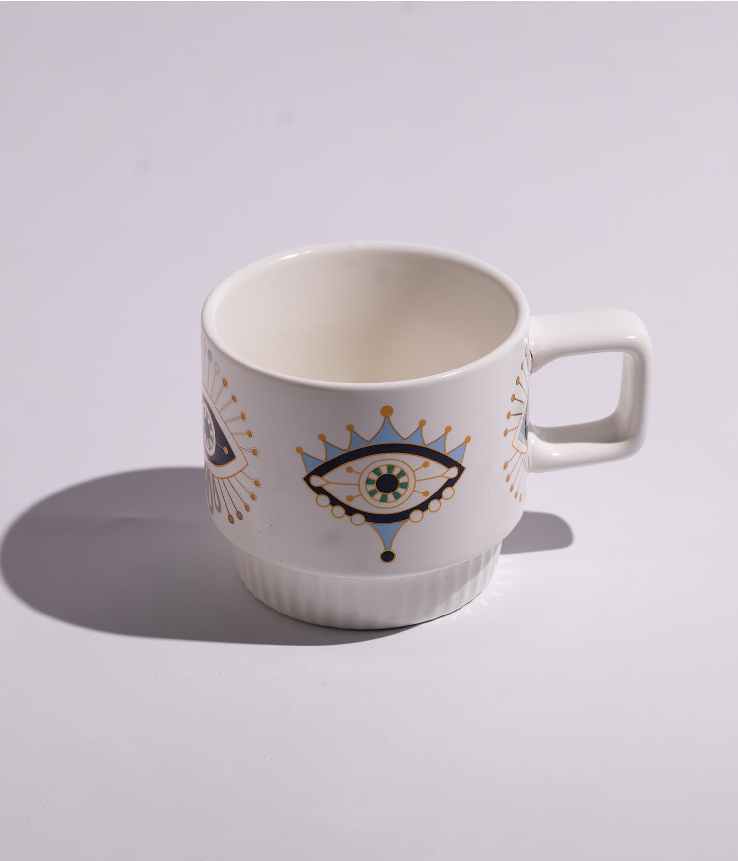 كوب مصنوع من السيراميك باللون الأبيض مزين برسوم عيون زرقاء بأشكال فنية مختلفة، مناسب للاستخدام اليومي مع القهوة أو الشاي