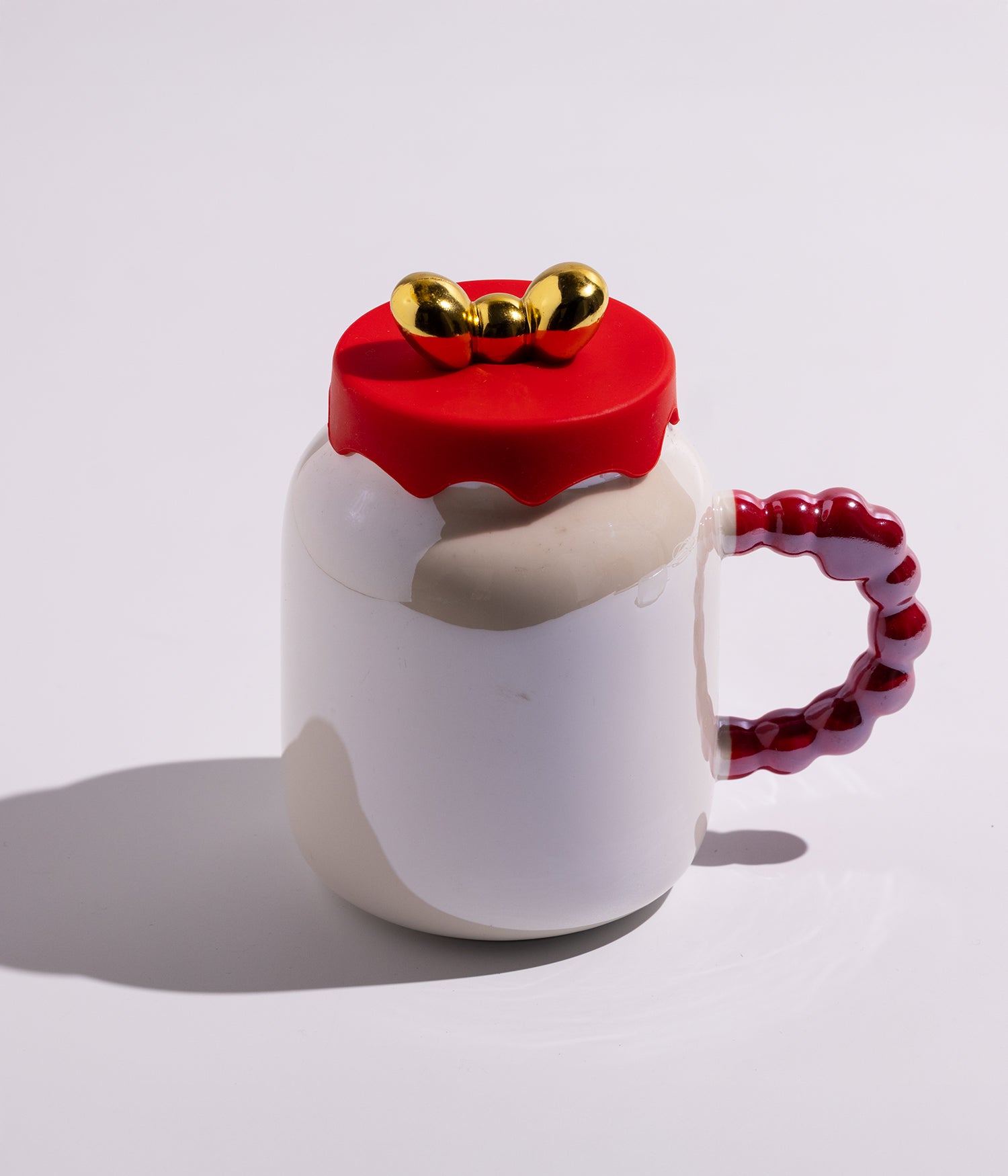 كوب سيراميكي أنيق باللون الأبيض، مزود بغطاء بتصميم فيونكة مميزة ومقبض مزين بقلوب ملونة، مناسب للقهوة أو الشاي ويعد خيارًا جميلًا للهدايا