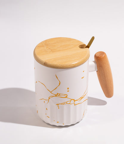 كوب سيراميكي باللون الأبيض مزخرف بعروق ذهبية أنيقة، يحتوي على مقبض وغطاء خشبي وملعقة، ملائم للاستخدام اليومي في المنزل أو المكتب