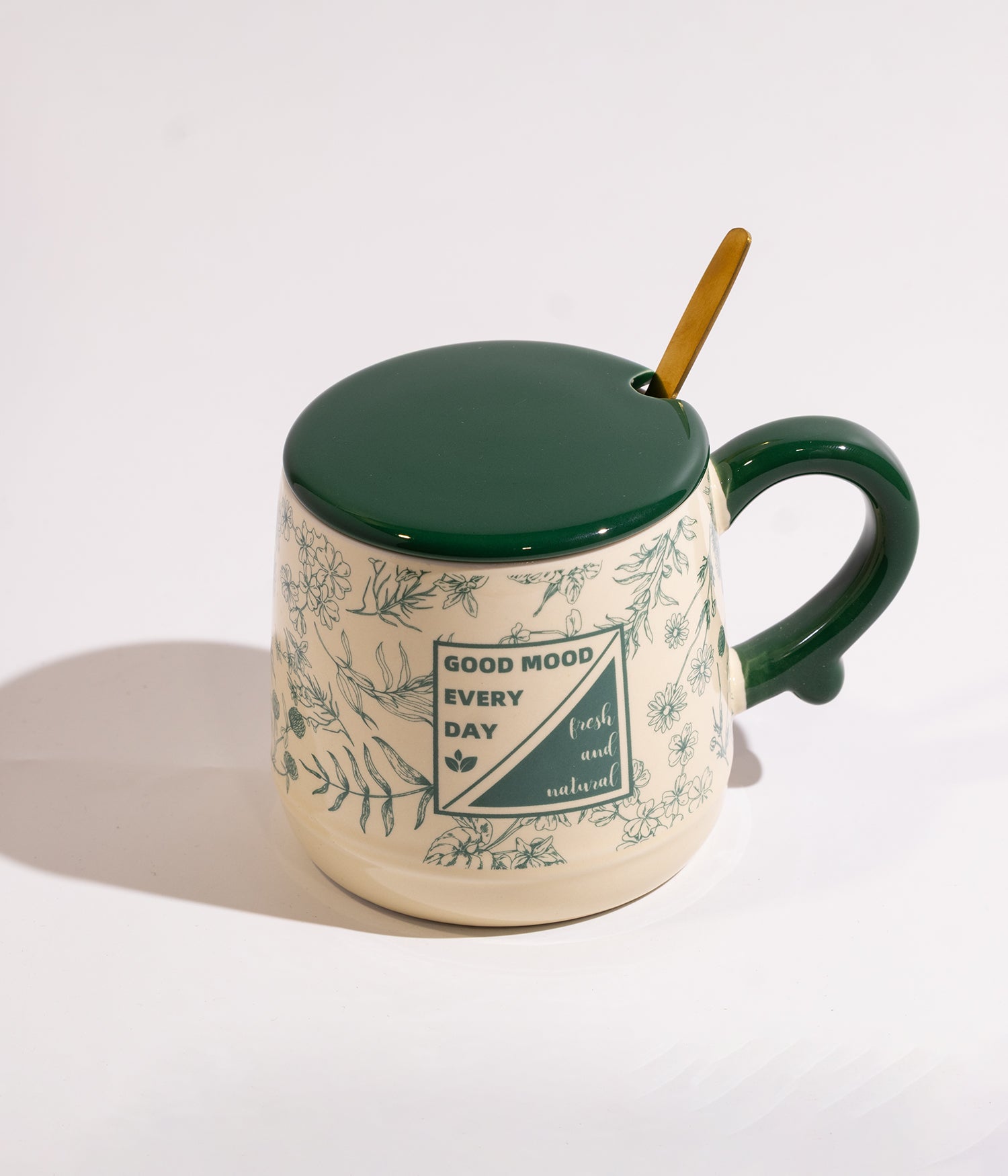 كوب مصنوع من السيراميك باللون الأبيض مزين بورود خضراء، مزود بغطاء وملعقة ذهبية، مناسب للاستخدام اليومي مع القهوة أو الشاي